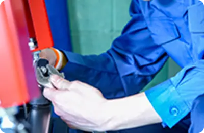 青い作業服を着た技術者が機械の部品を調整している様子。