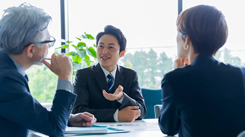 スーツ姿のビジネスパーソンがオフィスで商談や打ち合わせをしている様子