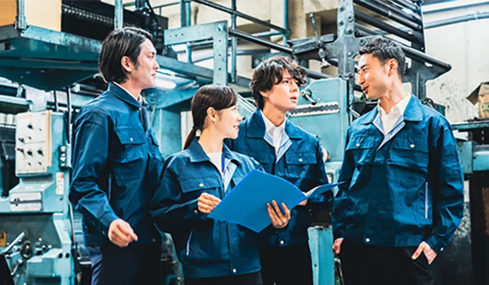 作業服を着たチームが工場内で打ち合わせをしている場面。