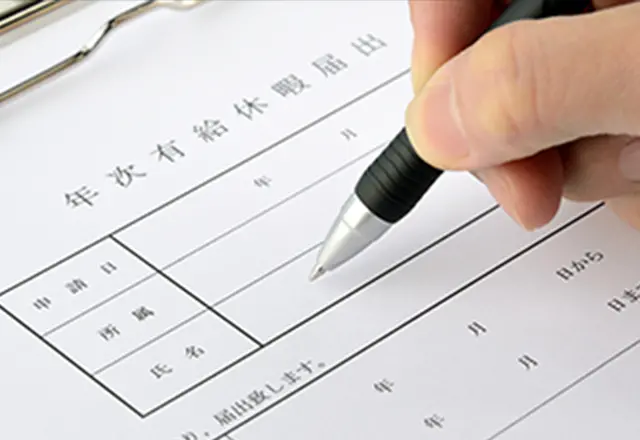 「年次有給休暇届出」と書かれた書類に、ペンで記入している場面。