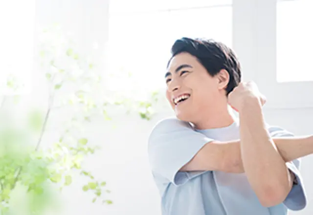 窓際でストレッチをしながら、笑顔でリフレッシュしている男性。