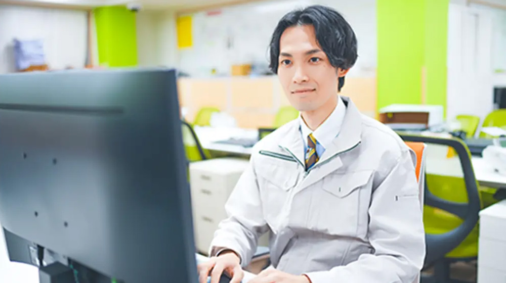 作業服を着た男性がデスクでパソコン作業をしている様子